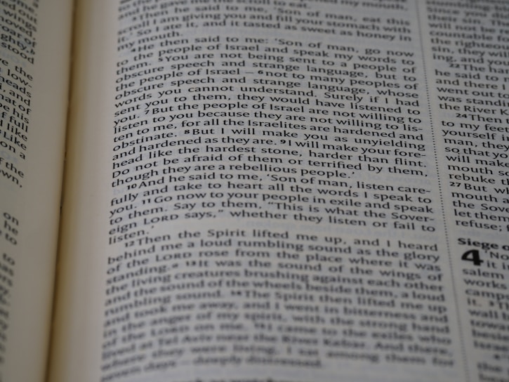 A close-up view of a page from a book, featuring text printed in a column layout. The text appears to be from a religious or philosophical work, with words and phrases presented in a structured format. The focus is on the middle of the page, with other text slightly blurred in the foreground and background.