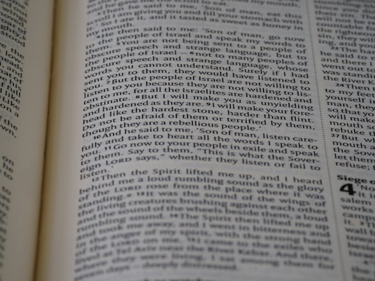A close-up view of a page from a book, featuring text printed in a column layout. The text appears to be from a religious or philosophical work, with words and phrases presented in a structured format. The focus is on the middle of the page, with other text slightly blurred in the foreground and background.