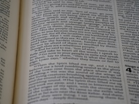 A close-up view of a page from a book, featuring text printed in a column layout. The text appears to be from a religious or philosophical work, with words and phrases presented in a structured format. The focus is on the middle of the page, with other text slightly blurred in the foreground and background.