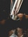 A close-up of a wristwatch with a sporty design. The watch is being worn on a wrist against a dimly lit backdrop featuring blurred patterns and lines. The lighting is subdued, creating a moody atmosphere.