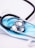 A stethoscope with black tubing is resting on top of a blue disposable face mask. The mask is set on a white surface, and the metallic part of the stethoscope reflects the surrounding light.