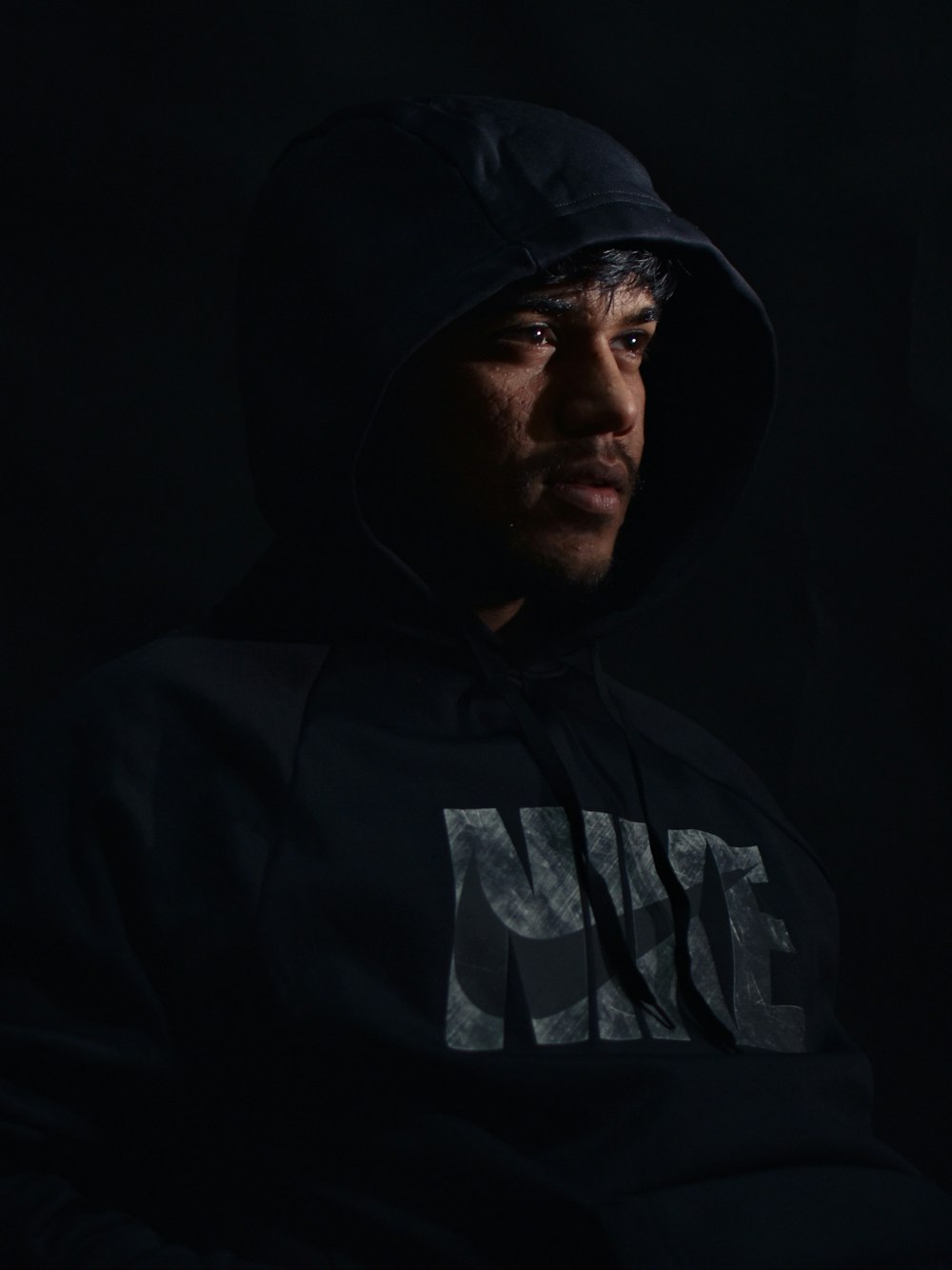 a man in a black hoodie sitting in a dark room