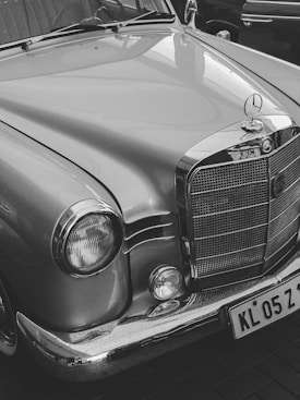 A classic car featuring a shiny chrome grill and headlight details, with smooth, curved lines and a distinct emblem on the hood.