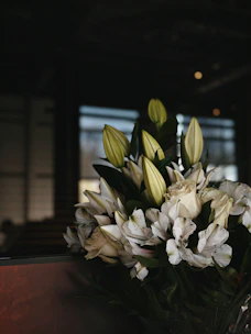 A delicate arrangement of white lilies and soft pink roses resting on a rustic wooden table, bathed in gentle natural light
