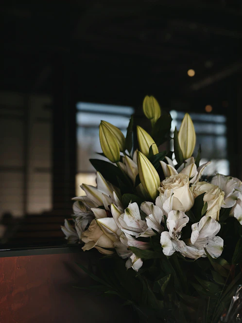 A delicate arrangement of white lilies and soft pink roses resting on a rustic wooden table, bathed in gentle natural light