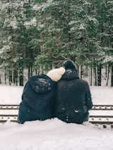 two people sitting on a bench in the snow