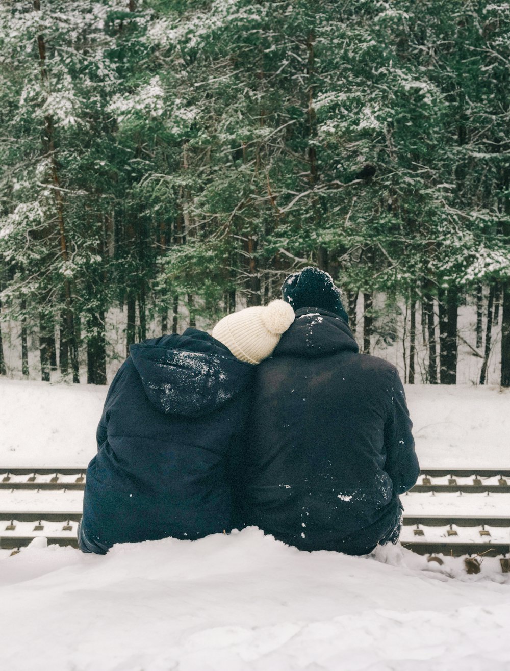 two people sitting on a bench in the snow