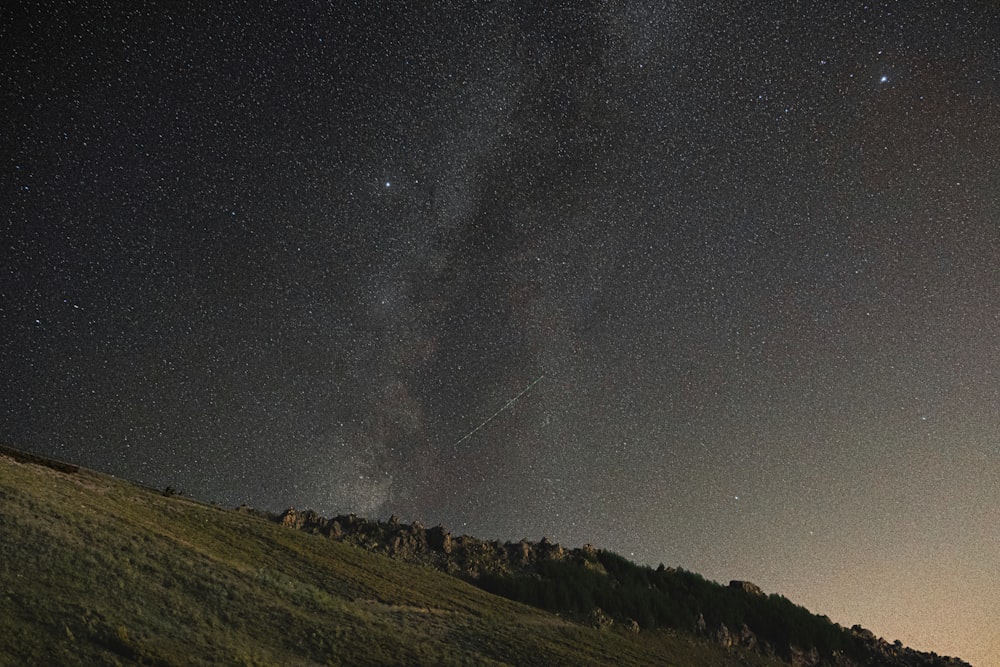 the night sky with stars above a grassy hill