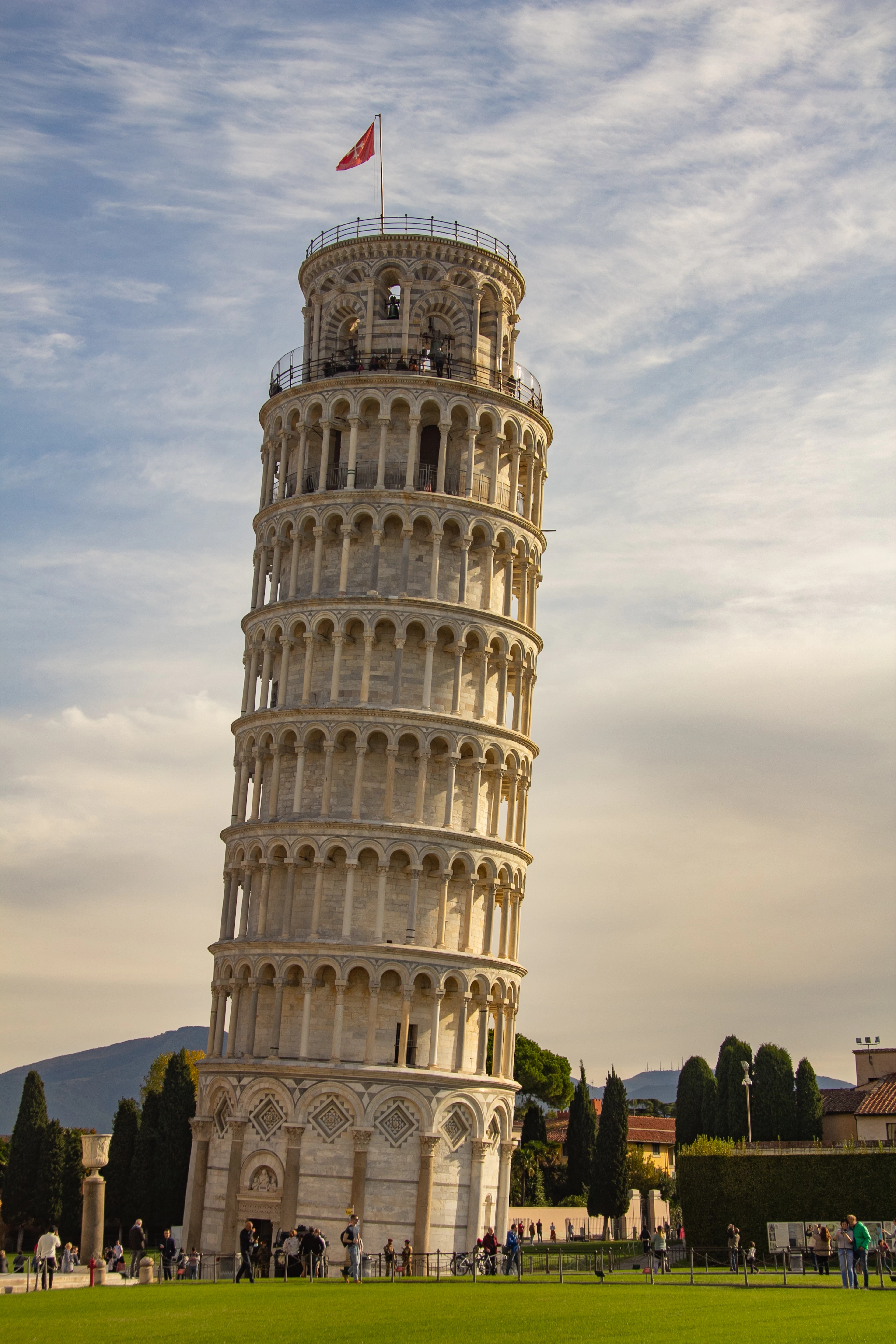 The Leaning Tower of Pisa glowing in warm golden-hour light with a dramatic sky and tourists gathered at its base.