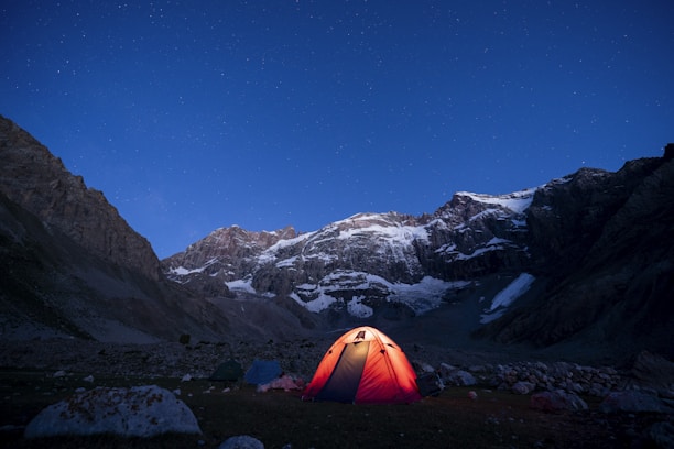 Campfire under starry Himalayan sky with tents and rugged peaks surrounding.