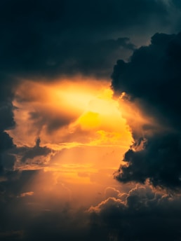 Dark, dramatic clouds part slightly to reveal a radiant burst of golden sunlight. The interplay between the shadows and light creates a mystical and awe-inspiring atmosphere.