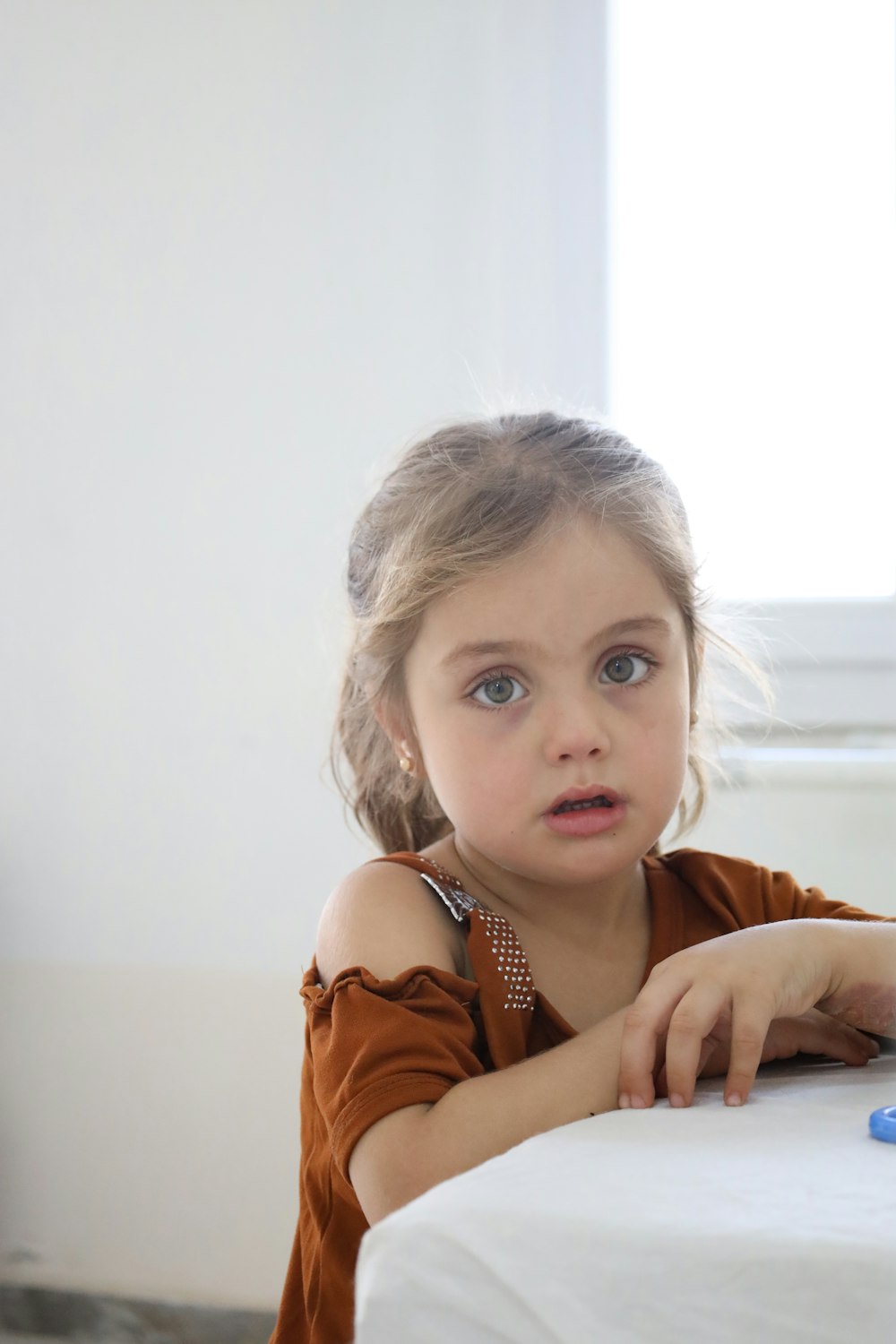 a little girl sitting at a table looking at the camera