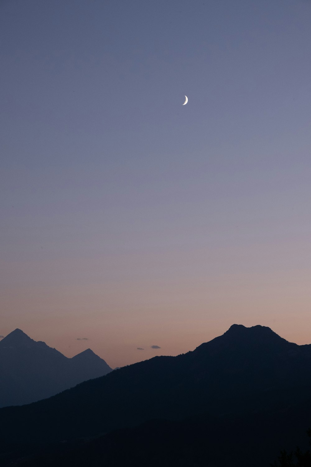 the moon is setting over a mountain range