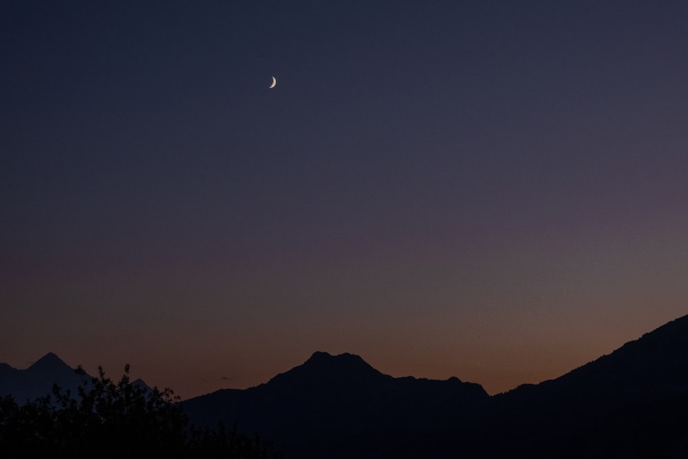 the moon is setting over a mountain range