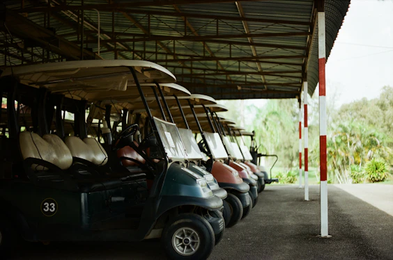 Row of golf carts parked under a covered shelter at a golf cart rental facility.