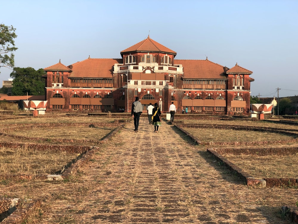 two people walking down a dirt road in front of a building