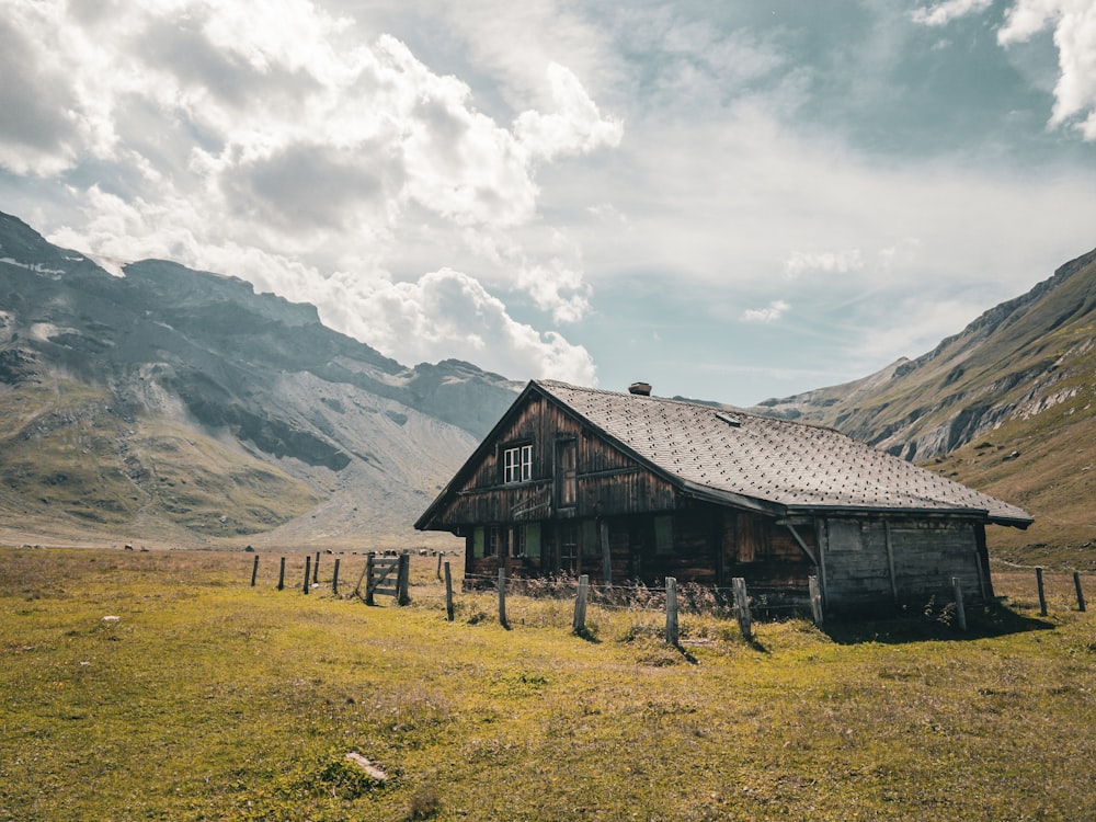 an old wooden house in a field with mountains in the background