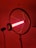 A lamp with a ring-shaped structure surrounding a bright red fluorescent tube, mounted on a stand in a dimly lit room. The lighting casts a warm, reddish glow throughout the space.