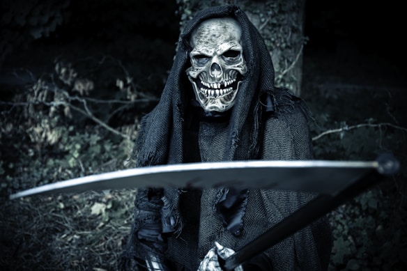 A grim reaper figure is prominently featured, wearing a tattered black hooded cloak and holding a large scythe. The skeletal face has a sinister grin, and the background is dark and forested, adding to the eerie atmosphere.