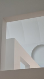 An abstract architectural composition featuring geometric shapes and lines with a soft interplay of light and shadow. The image includes arching and rectangular forms creating a minimalist and serene atmosphere.