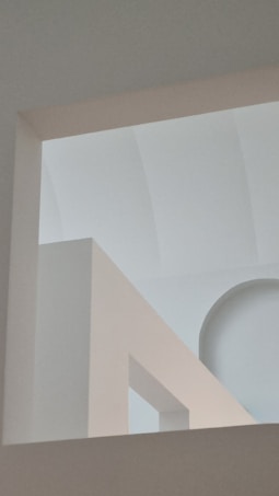 An abstract architectural composition featuring geometric shapes and lines with a soft interplay of light and shadow. The image includes arching and rectangular forms creating a minimalist and serene atmosphere.