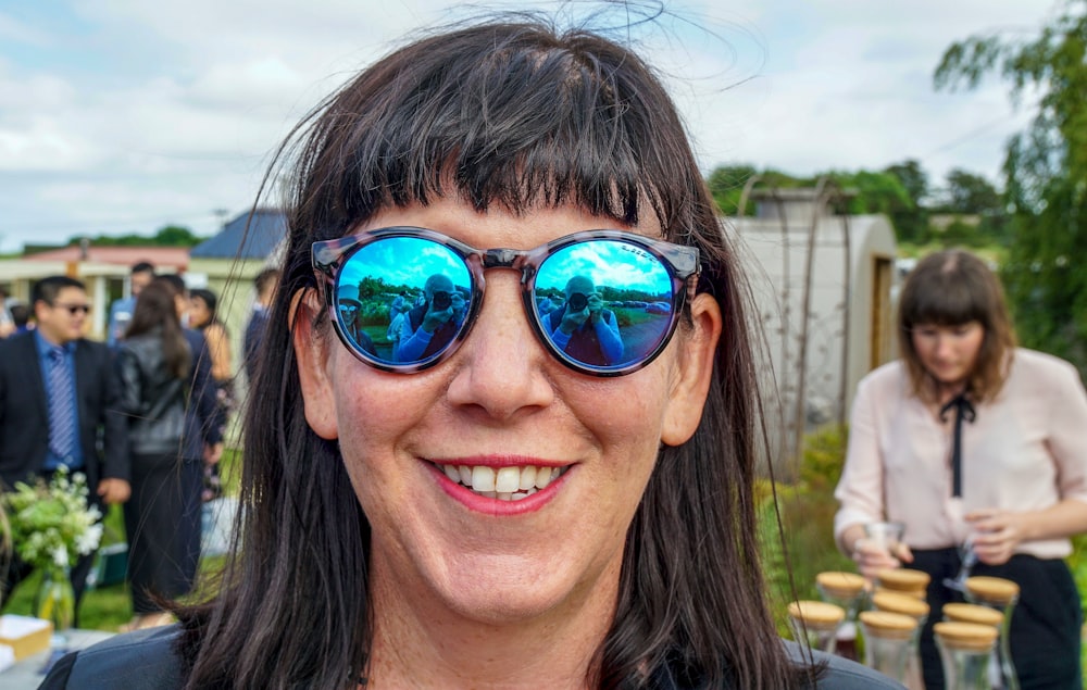 a woman wearing blue mirrored sunglasses standing in front of a group of people