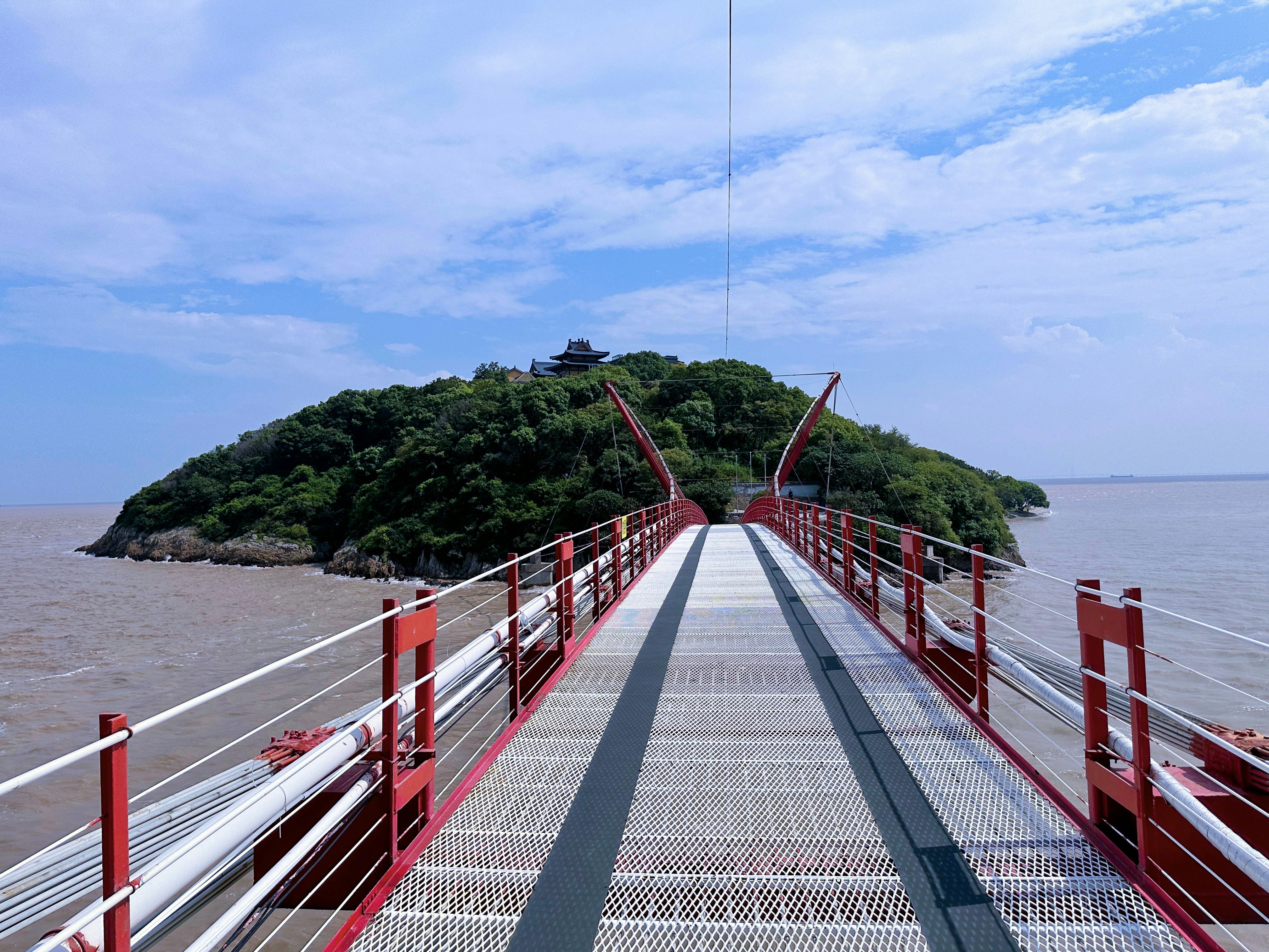 a long red bridge with a small island in the background