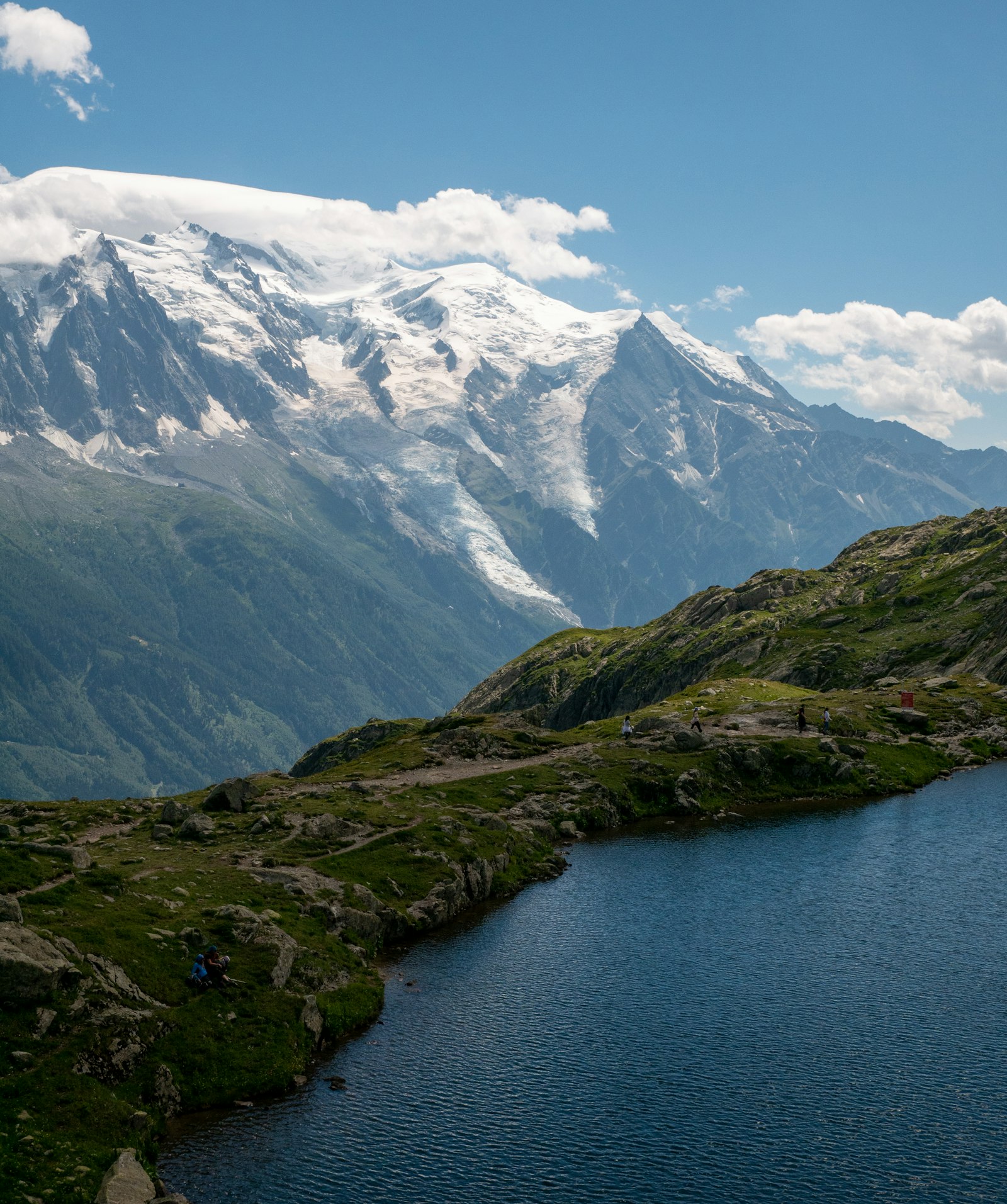 Hikers beside an alpine lake below the snow-covered Mont Blanc massif on the Tour du Mont Blanc