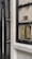 An ornate door with a black metallic frame, partially opened, reveals a brass intercom system embedded in the wall. The stone wall appears textured and there is a small plaque above the intercom.