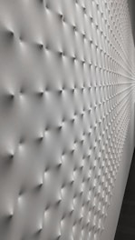 A wall with a geometric pattern of small protrusions, creating a textured effect with soft lighting that enhances the depth and three-dimensional appearance. The surface transitions smoothly, giving a modern and minimalistic look.