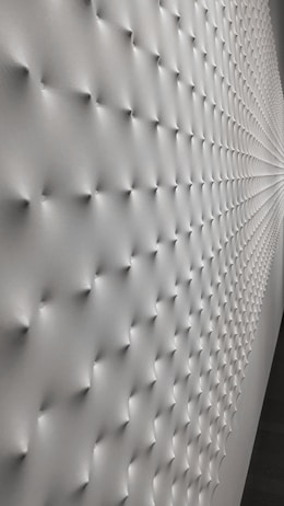 A wall with a geometric pattern of small protrusions, creating a textured effect with soft lighting that enhances the depth and three-dimensional appearance. The surface transitions smoothly, giving a modern and minimalistic look.