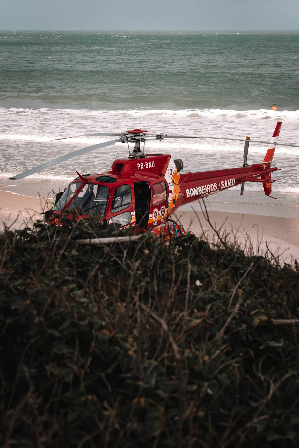 a red helicopter sitting on top of a sandy beach