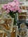 A lavish display featuring a bouquet of pink and white flowers in the center, surrounded by an assortment of sweets and nuts presented in ornate, decorative containers. The setup includes clear glass and metallic elements, giving a luxurious and festive appearance.