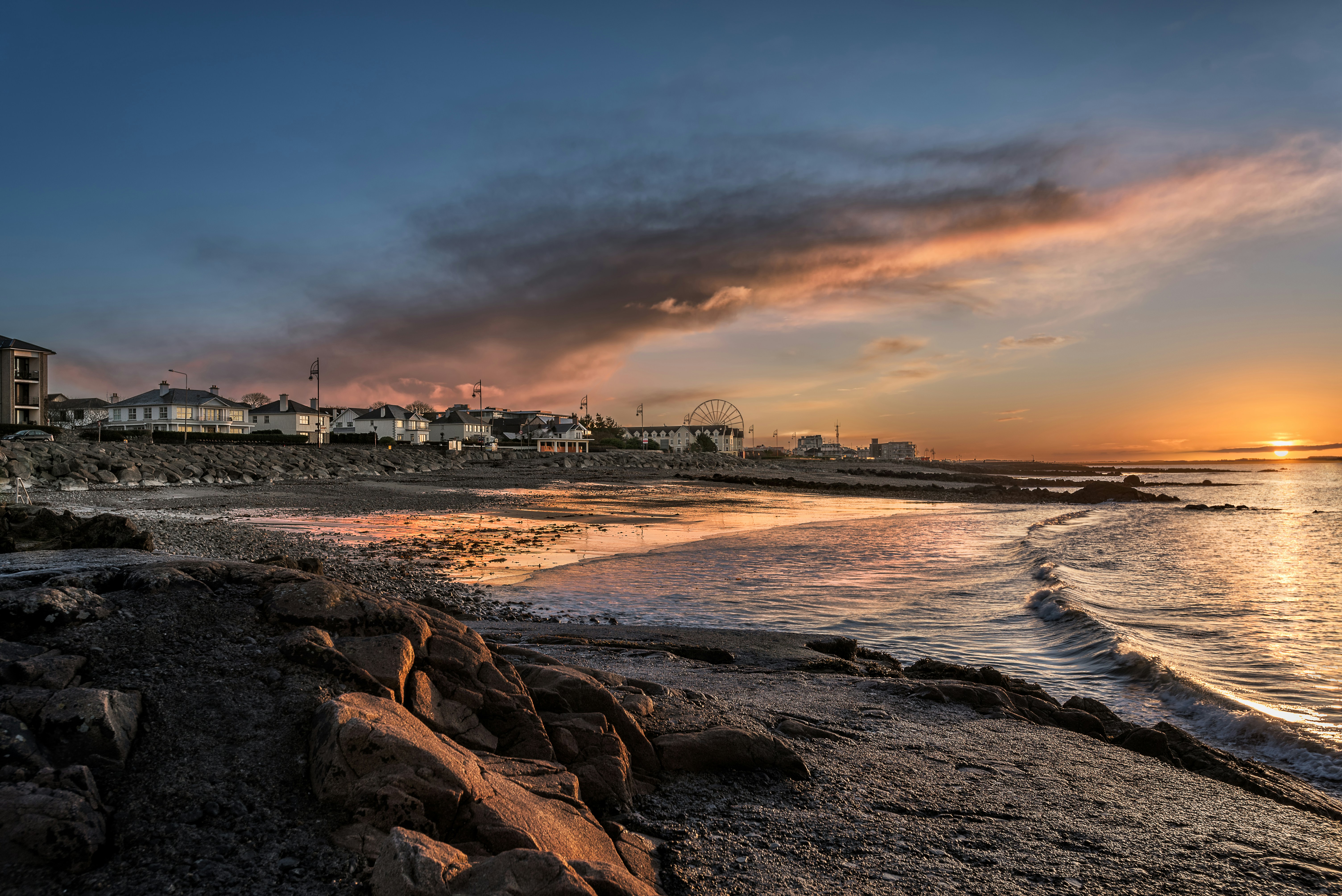 the sun is setting over a beach with houses in the background