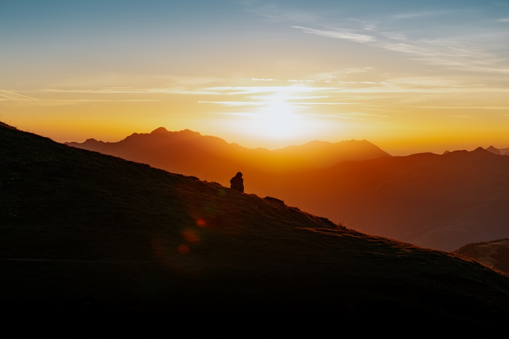 a person sitting on top of a hill at sunset