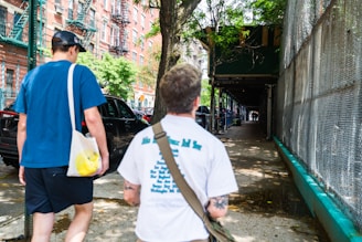 a couple of men walking down a street next to a fence