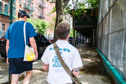 a couple of men walking down a street next to a fence