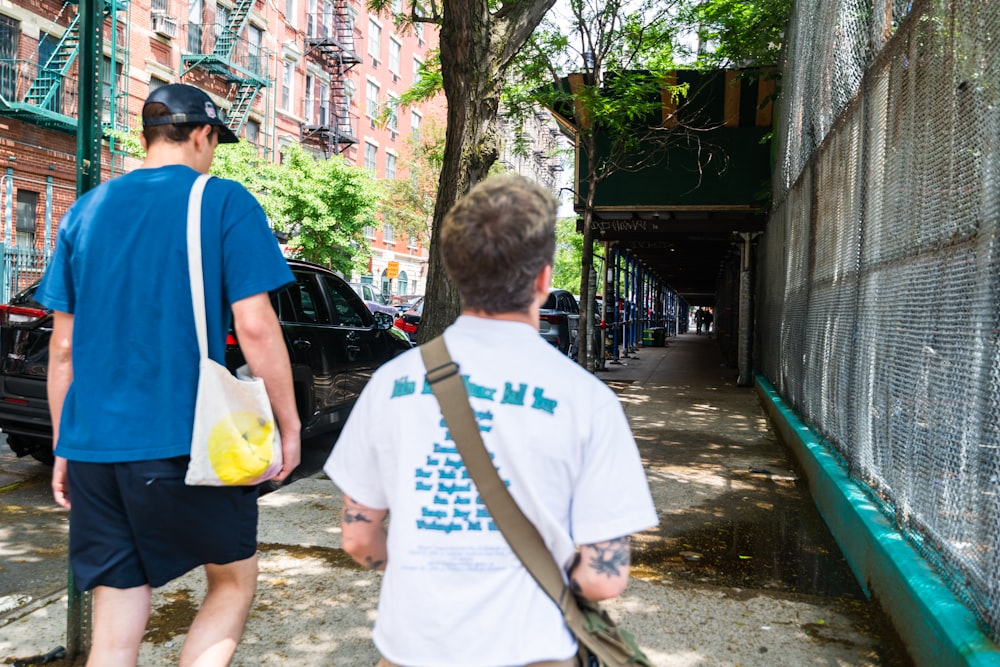 a couple of men walking down a street next to a fence