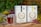 Two tins of Sunbird Rooibos tea are placed on a wooden surface surrounded by colorful flowers. There are two glasses of rooibos tea in the foreground, and lush green foliage is visible in the background. The scene is set outdoors, giving a fresh and natural vibe.