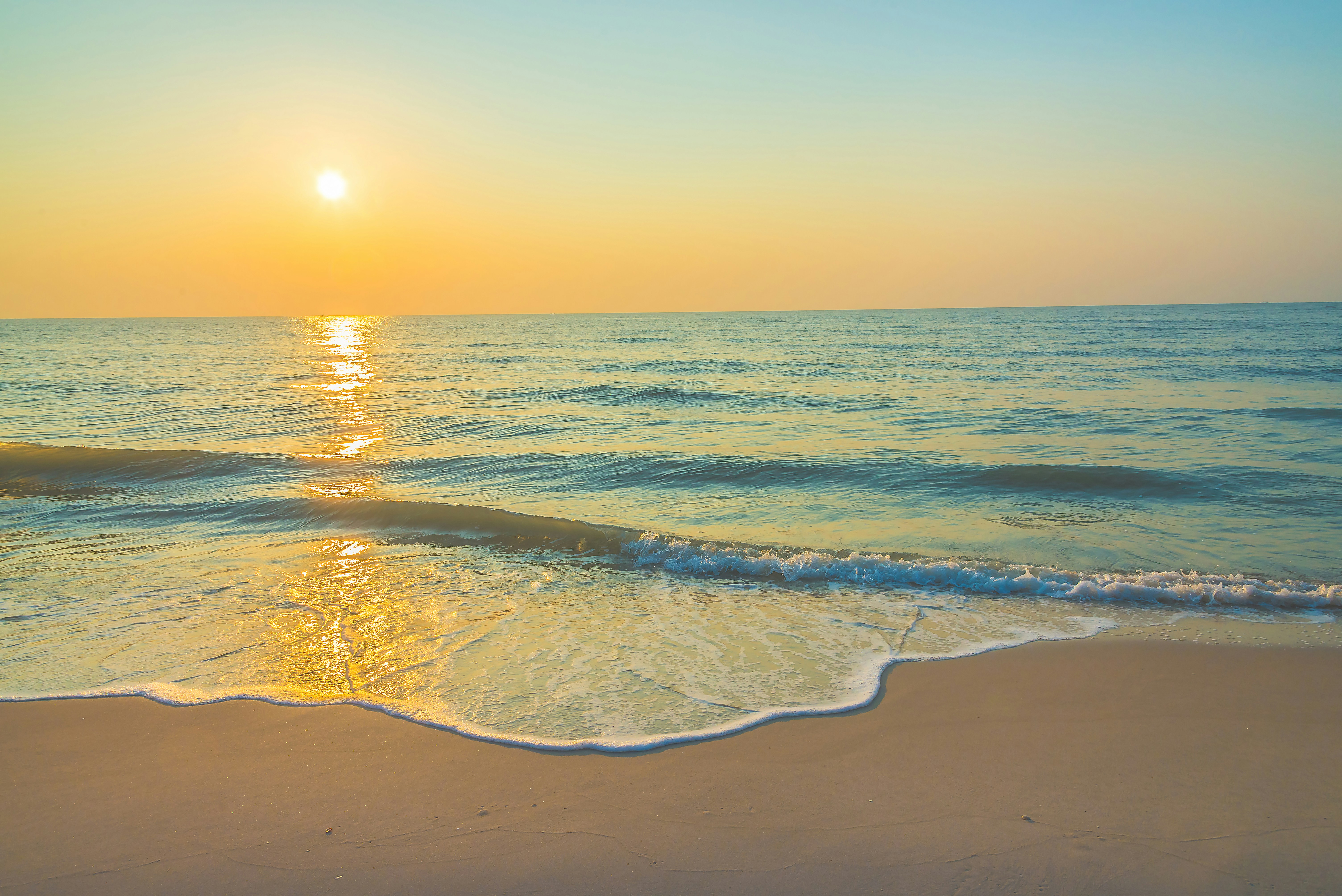 Sunset over a calm beach with golden light reflecting on the water.