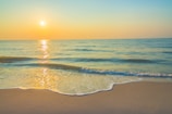 Sunset over a calm beach with golden sand and gentle waves lapping the shore.