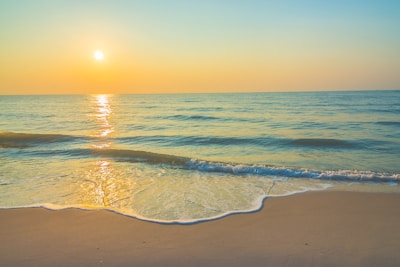 Sunset over a calm beach with golden sand and gentle waves lapping the shore.