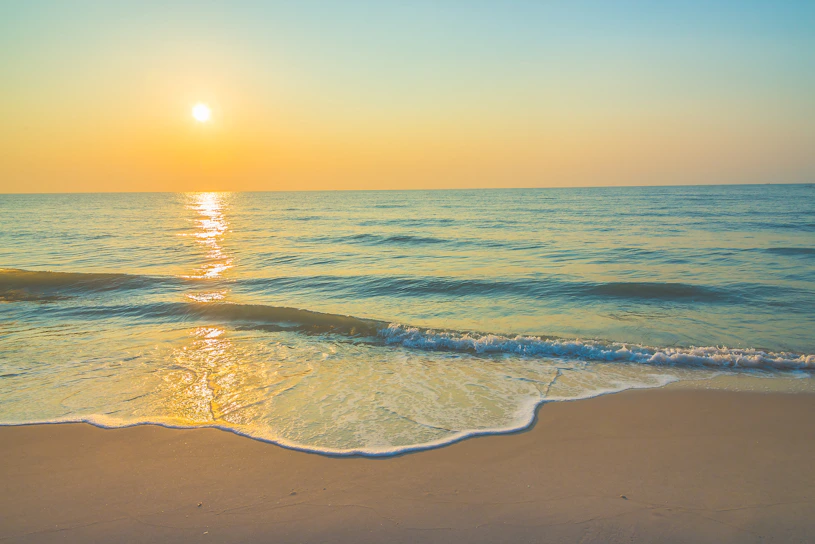 A breathtaking sunset over a calm tropical beach with golden skies and gentle waves.