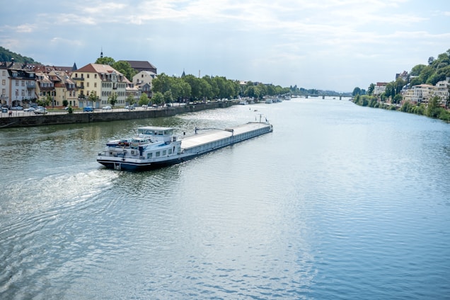 A 50% full-frame shot of the blue, white, and black Kempenaar barge named Libertas gently sailing on a calm river.