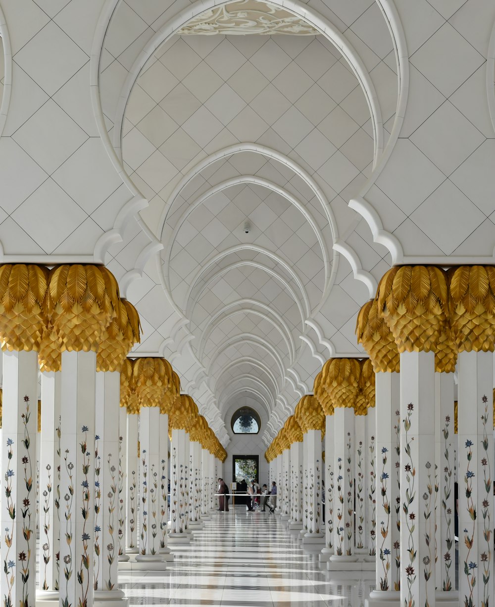 um longo corredor com colunas brancas e douradas