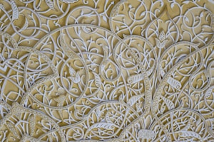 Intricate white arabesque patterns with floral and vine motifs against a light yellow background, showcasing elaborate curvilinear designs.
