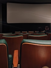 A dimly lit movie theater with shadowy figures watching a horror film, flickering light casting eerie glows.