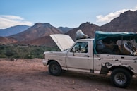 Old car being loaded onto a flatbed truck with green mountains in the background.