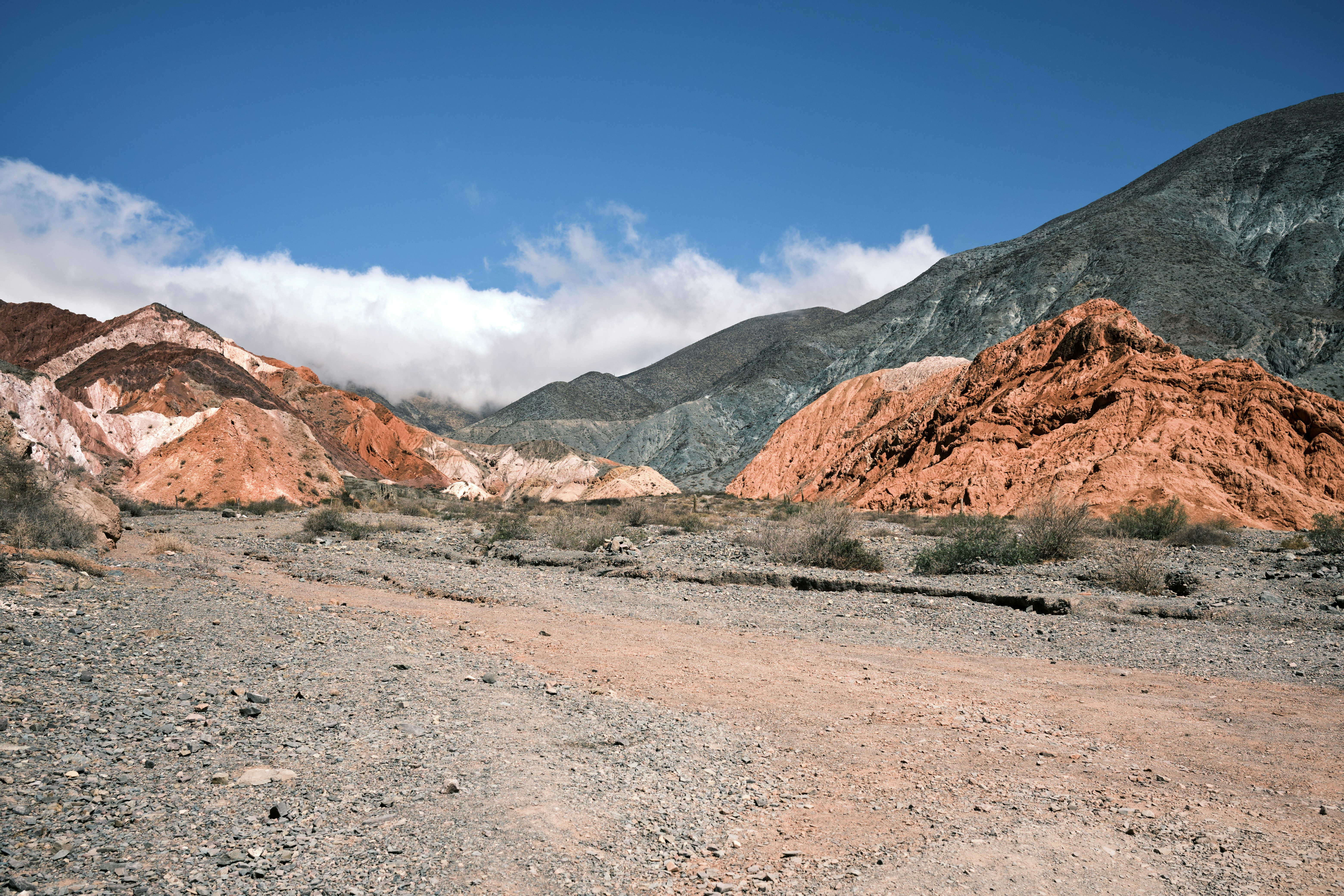 a dirt road surrounded by mountains under a blue sky