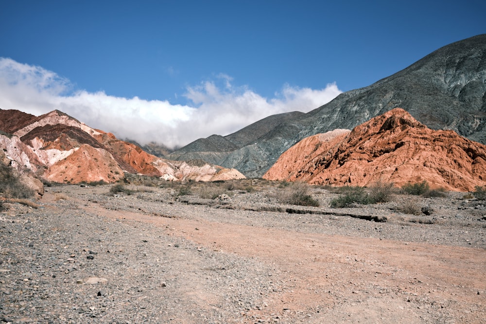 a dirt road surrounded by mountains under a blue sky